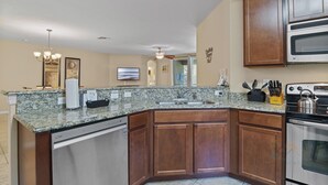 A kitchen with granite countertops, wooden cabinets, a dishwasher, a stove, and a microwave. - Tranquil Terrace - 10 Mins to Disney! (Kissimmee)