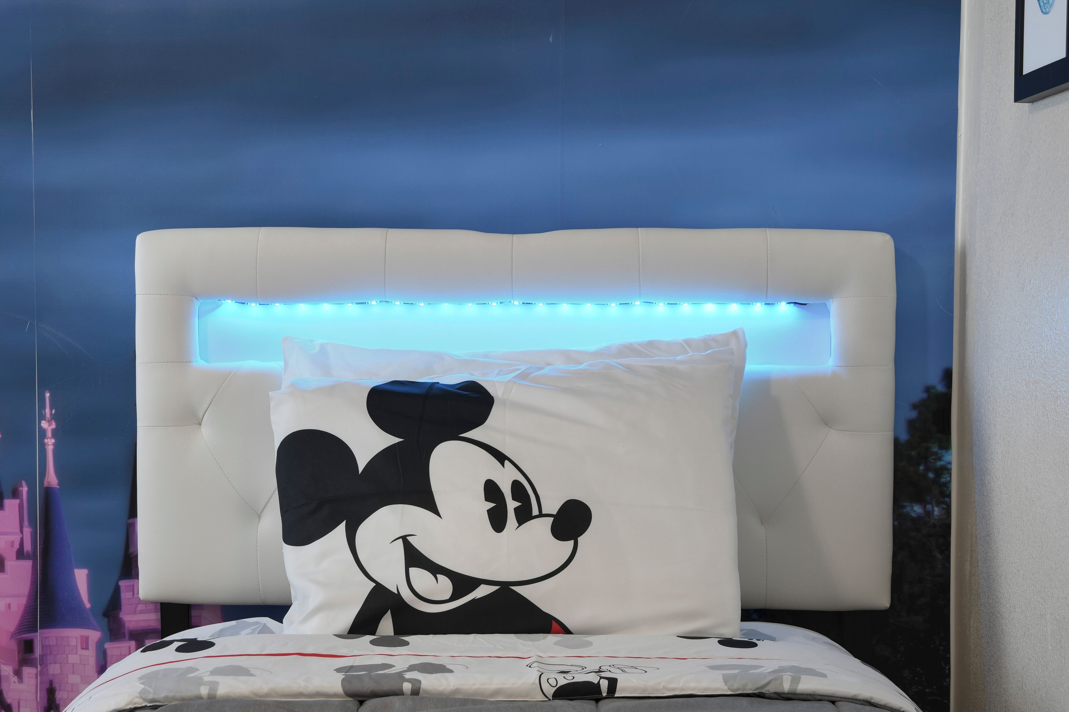 A bed with a Mickey Mouse pillow, a headboard with LED lights, and a castle-themed wall.