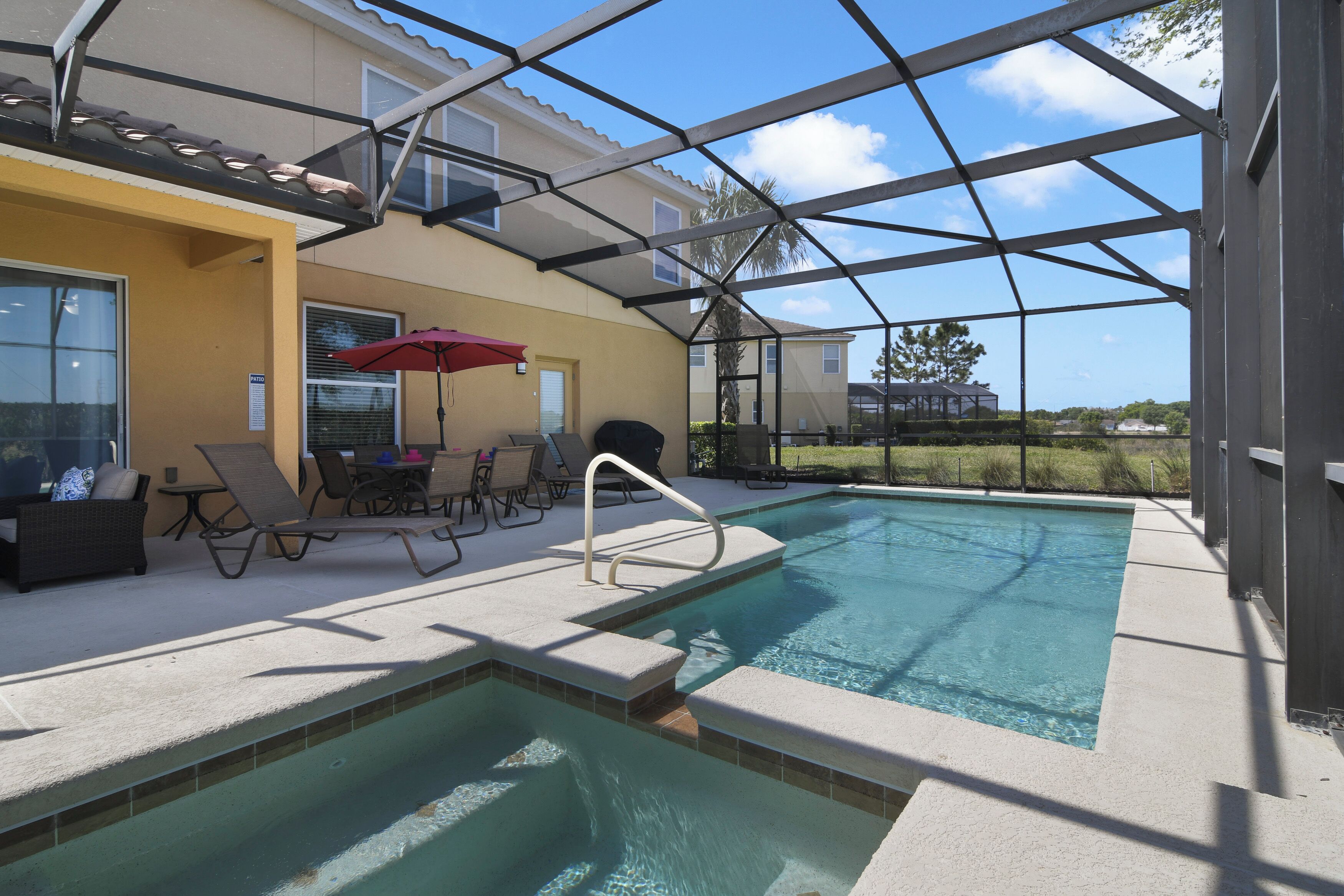 A covered outdoor pool area with lounge chairs and a red umbrella.