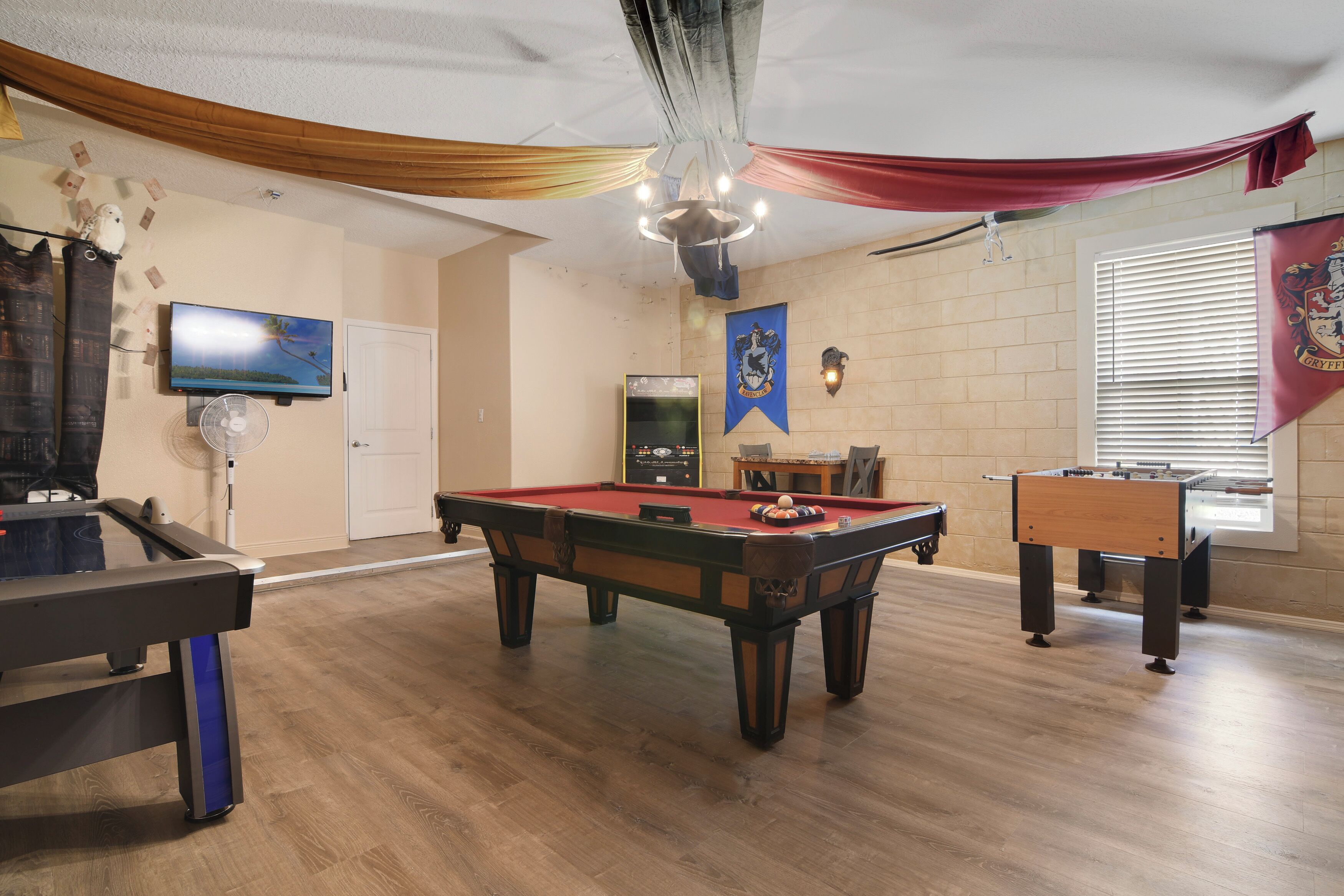 A pool table, a foosball table, and a television in a room with wooden floors and walls.