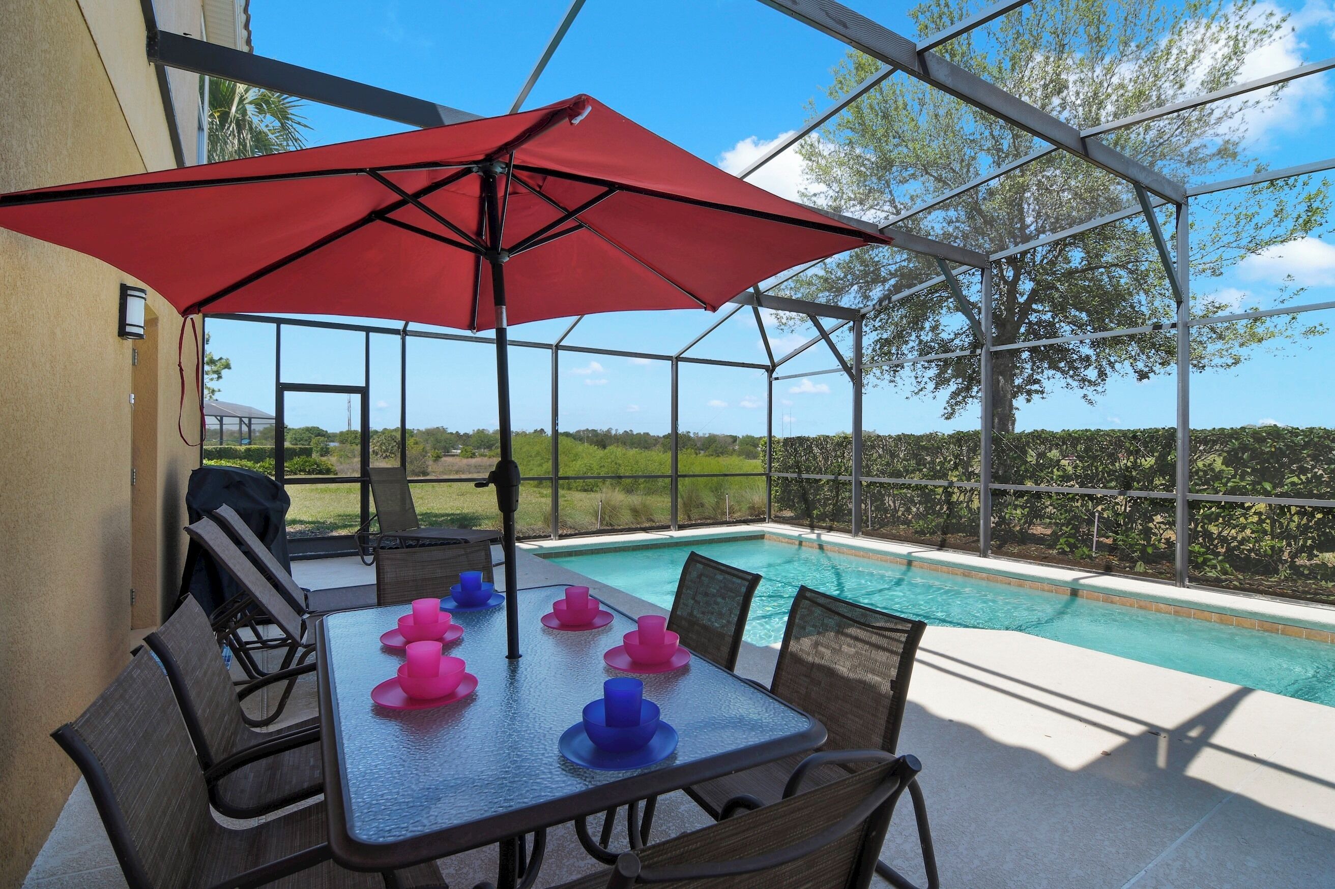 A covered outdoor area with a pool, dining table, chairs, and a red umbrella.