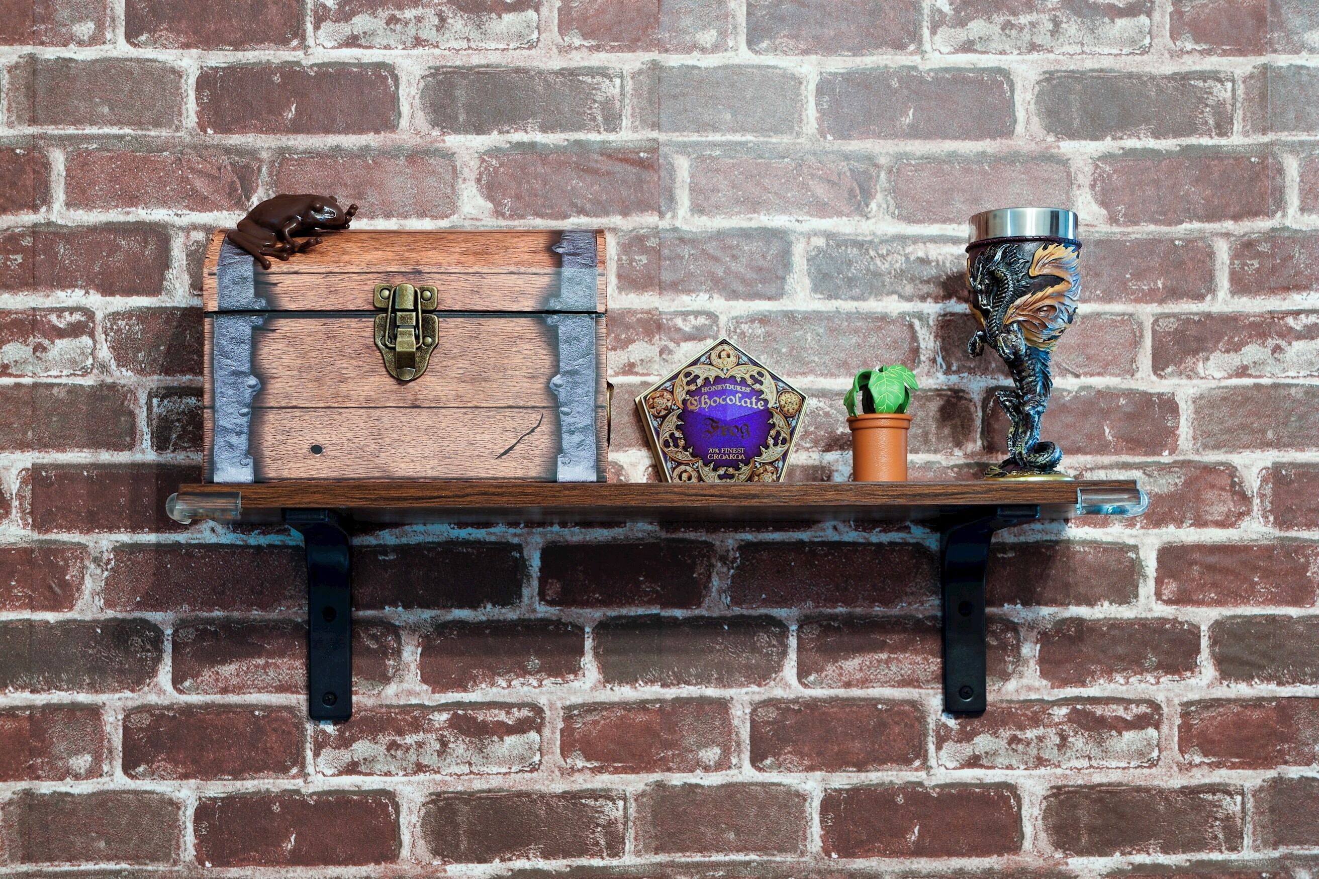 A wooden chest with a latch, a chocolate bar, a small potted plant, and a decorative item on a shelf against a brick wall.