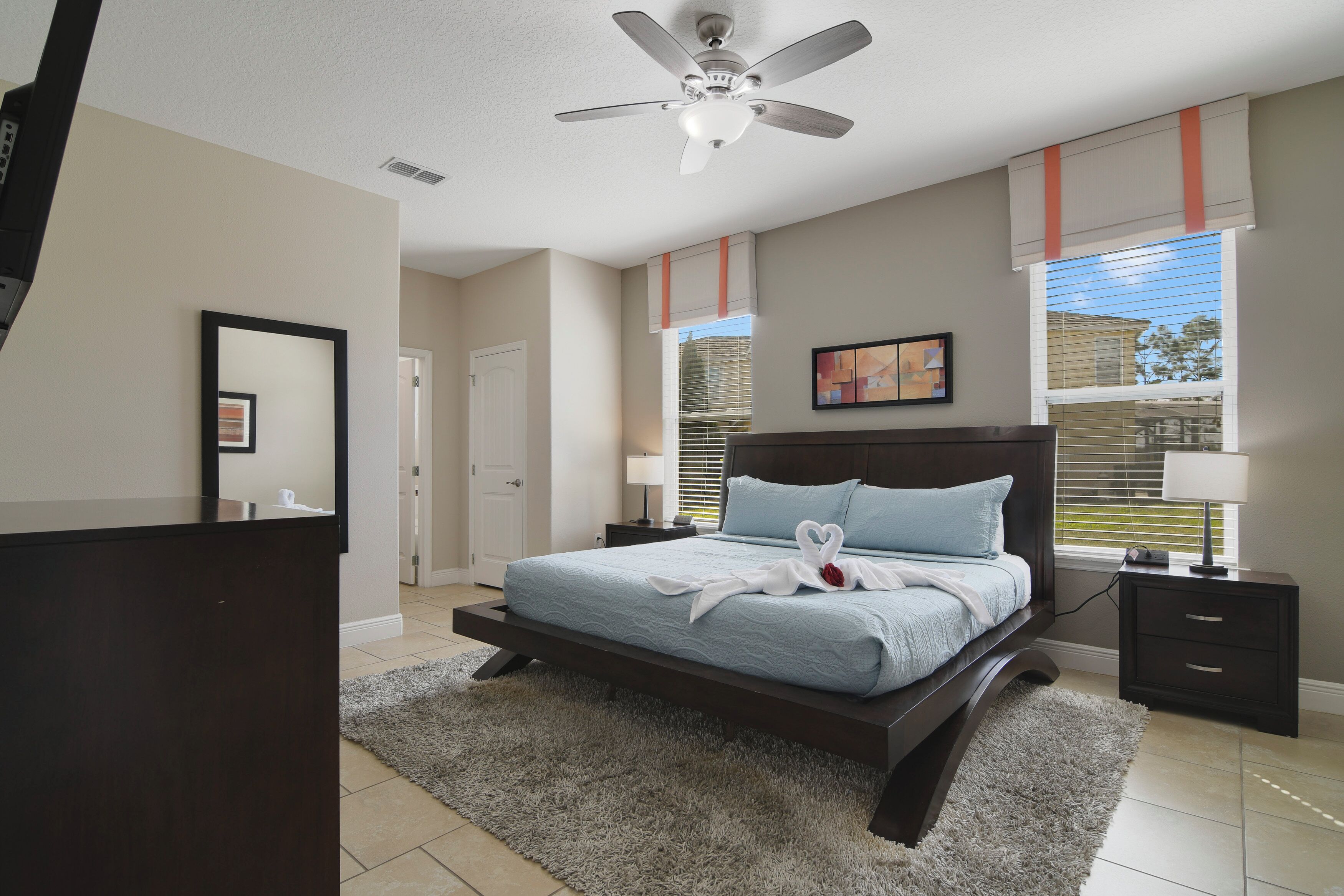 A bedroom with a bed, a ceiling fan, a nightstand, a dresser, and a window with blinds.