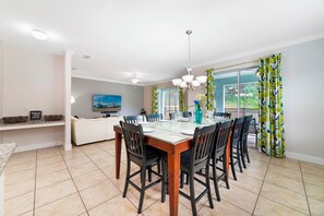 A dining area with a glass-top table, black chairs, a chandelier, and a view through large windows. - Theatre & Games - Luxe Resort +10 Min Disney +pets (Kissimmee)