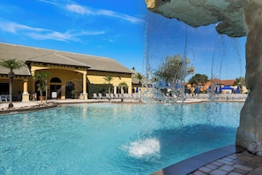 A swimming pool with a water feature, a building with a tiled roof, and palm trees. - Theatre & Games - Luxe Resort +10 Min Disney +pets (Kissimmee)