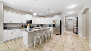 Une cuisine moderne avec des meubles blancs, un îlot central doté de tabourets, un réfrigérateur et un four à micro-ondes.