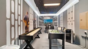 Une pièce avec une table de baby-foot, une table de ping-pong et un grand tableau accroché au mur.