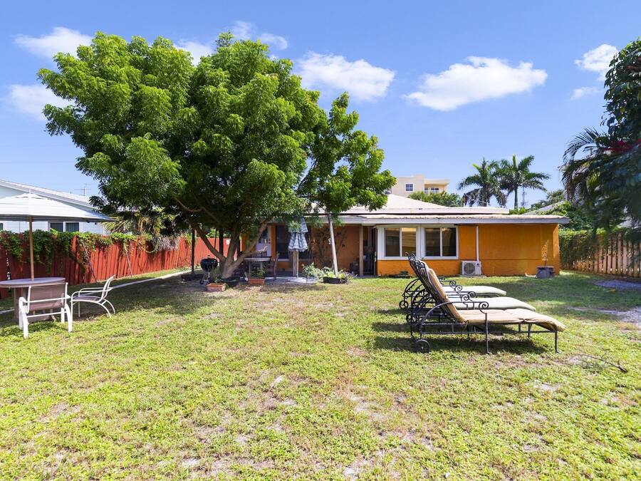 Uma casa com quintal cercado, uma árvore e móveis de jardim.