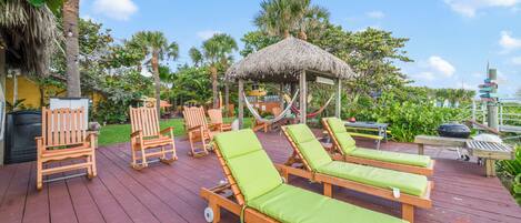 A wooden deck with lounge chairs and a thatched-roof gazebo.
