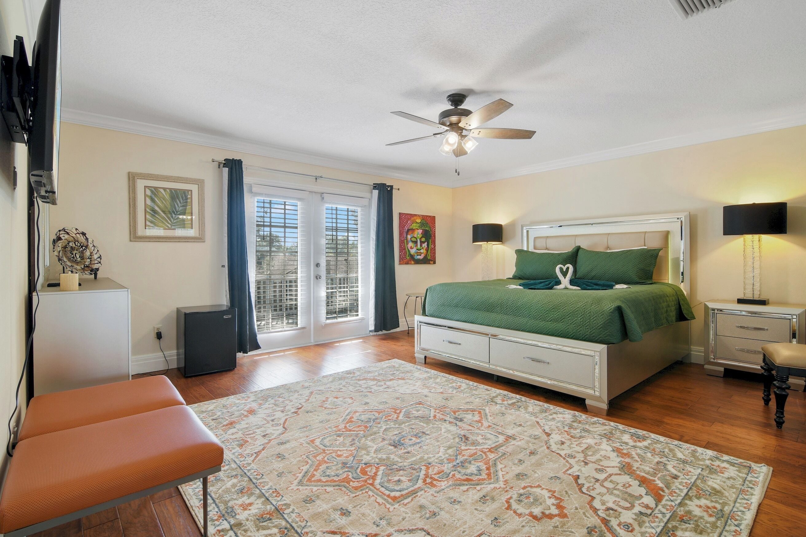 A bedroom with a bed, a ceiling fan, a nightstand, a bench, and a view through the glass doors.