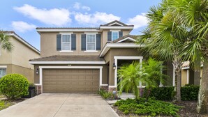A two-story house with a garage, a small porch, and a well-maintained lawn with palm trees. - Sunset Arcade - Large Pool/spa + Luxe Resort +pets (Davenport)