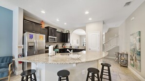 A kitchen with a central island, dark cabinets, stainless steel appliances, and a white door leading to another room. - Sunset Arcade - Large Pool/spa + Luxe Resort +pets (Davenport)