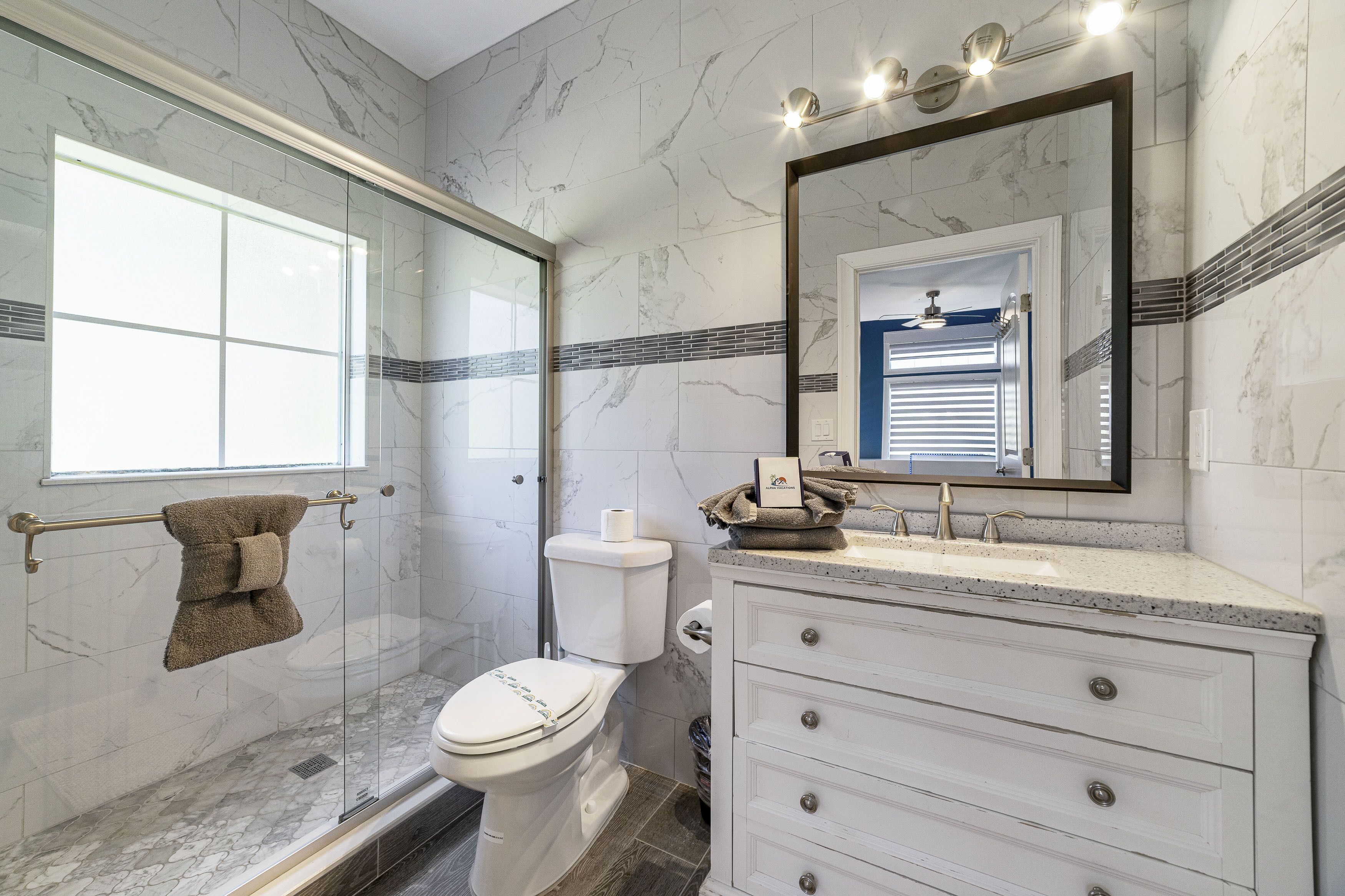 Un baño con cabina de ducha de vidrio, inodoro, lavabo con espejo y tocador con cajones.