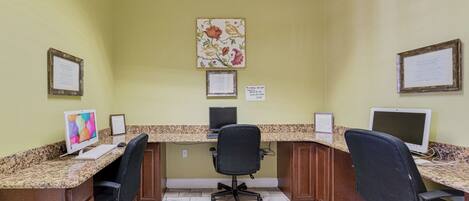 Un área de recepción con dos monitores de ordenador, un ordenador de escritorio, una silla de oficina negra, certificados enmarcados en la pared y una obra de arte floral.