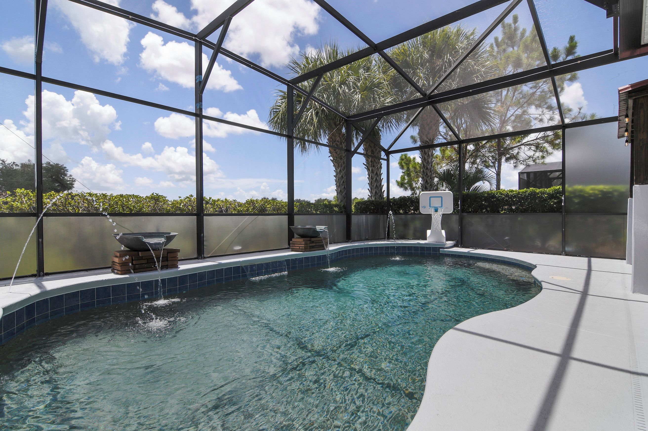 A swimming pool with a glass enclosure, clear water, and a basketball hoop.