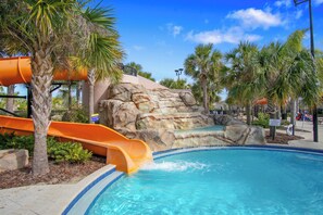 A pool area with a water slide, palm trees, and a rocky waterfall backdrop. - The Charming Chateau - Luxe - Resort - Location (Davenport)