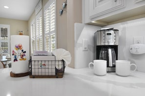 A kitchen with a coffee maker, two white mugs, a basket with a Mickey Mouse design, and a tissue roll. - The Charming Chateau - Luxe - Resort - Location (Davenport)
