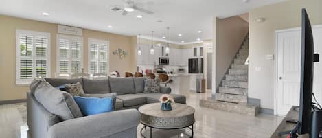 A spacious living room with a gray sectional sofa, a round coffee table, and a flat-screen TV on a wooden stand.