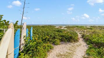 A sandy path leading to the beach with surfboards leaning against a fence.