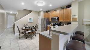 A kitchen with wooden cabinets, a stainless steel refrigerator, a microwave, and a stove. There is a dining table with chairs and a kitchen island with stools. - Serenity - Family & Pet Friendly, Amazing Location (Kissimmee)