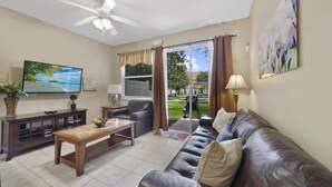 A living room with a leather sofa, a wooden coffee table, a TV, and a ceiling fan. - Serenity - Family & Pet Friendly, Amazing Location (Kissimmee)