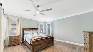 Ein Schlafzimmer mit Bett, Deckenventilator, Kommode und einem Fenster mit Jalousien.