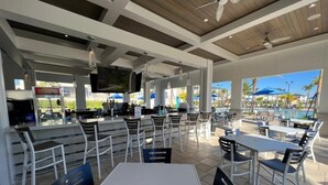 An outdoor dining area with tables and chairs, a bar area with a television, and a pool in the background. - Champions Oasis - Resort&arcade -walk to Clubhouse (Davenport)