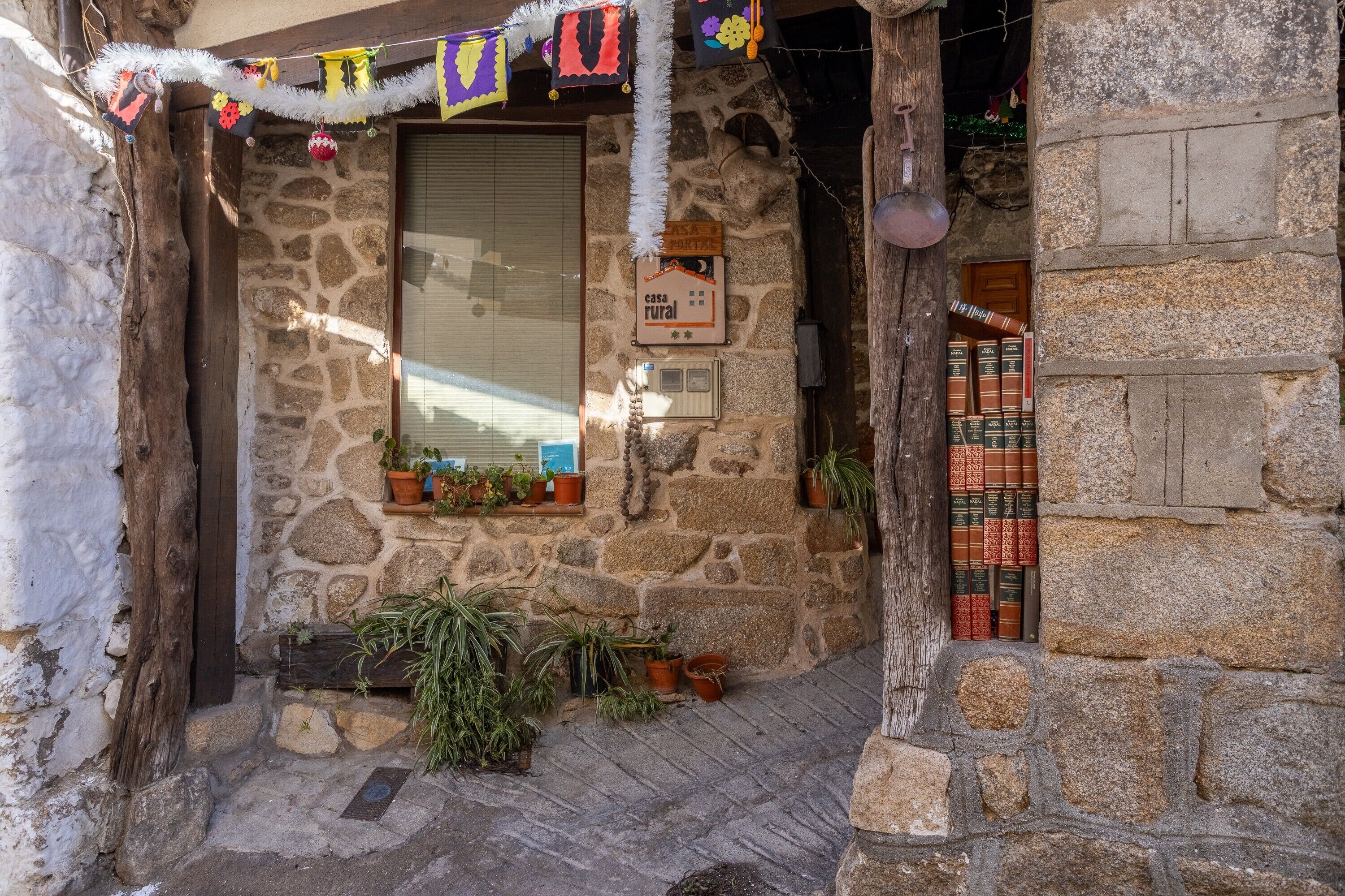 Un bâtiment rustique en pierre, doté d’une porte en bois, de plantes en pot et d’une enseigne indiquant qu’il s’agit d’une maison de campagne.