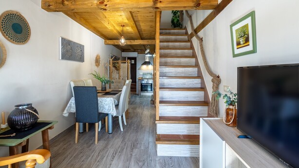 Un escalier en bois menant à un deuxième étage, un coin repas avec une table et des chaises, et un téléviseur posé sur un meuble.