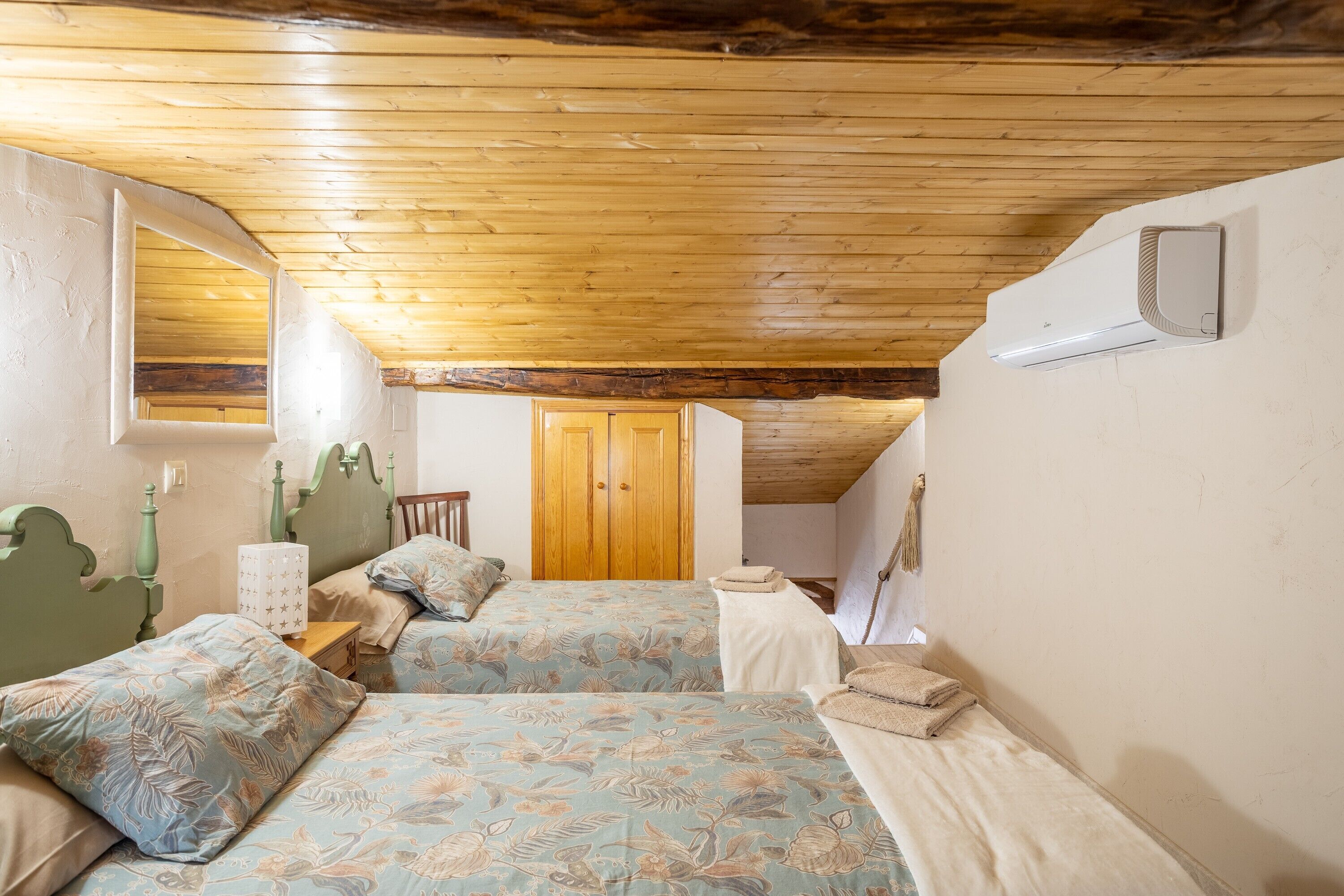 A bedroom with two beds, a wooden ceiling, a window, and a door.