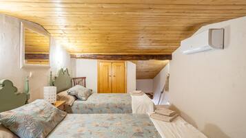 A bedroom with two beds, a wooden ceiling, a window, and a door.