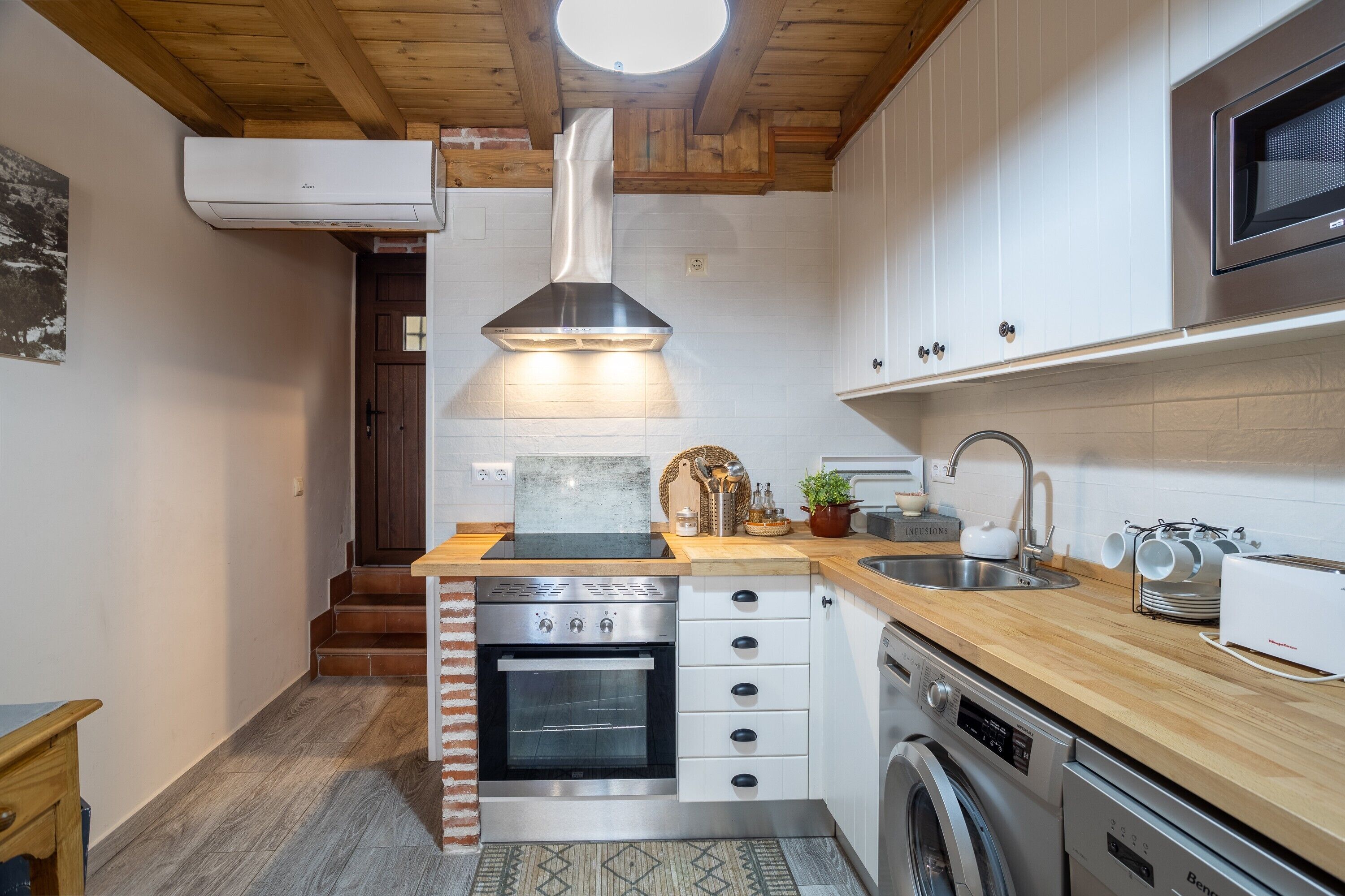 Une cuisine compacte dotée d’un four, d’un micro-ondes et d’un lave-linge encastrés, de plans de travail en bois et d’une fenêtre située au-dessus de l’évier.
