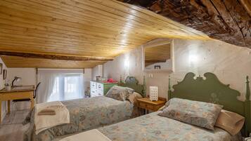 A room with two beds, a wooden ceiling, a desk, and a dresser.