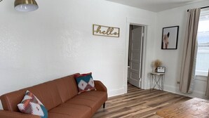 Een woonkamer met een bruine leren bank, een houten salontafel en een bord met de tekst 'hello' aan de muur.