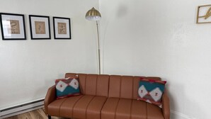 Een bruine leren bank met kussens met een patroon, een vloerlamp en lijstwerken aan de muur.