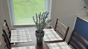 Uma mesa de jantar com quatro cadeiras, uma planta em vaso no centro e dois jogos americanos.