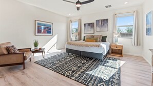 Een slaapkamer met een bed, nachtkastje, stoel, plafondventilator en een raam met gordijnen.