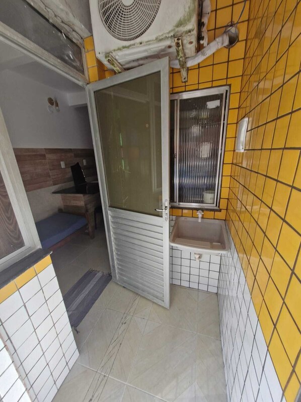 A bathroom with yellow tiled walls, a sink, and a window. - Apartamentos Itapuã Praia (Salvador)