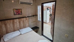 Ein Hotelzimmer mit Bett, Nachttisch, Klimaanlage und einer Tür zu einer Küchenzeile.