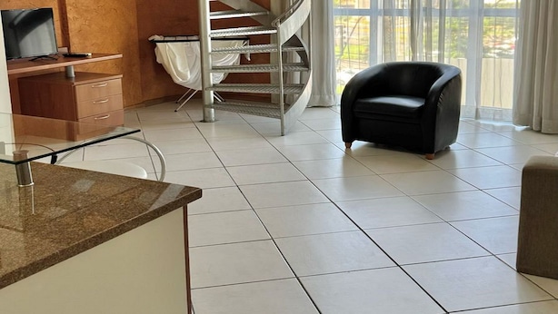 A spacious living area with a spiral staircase, a black leather chair, and a large window offering a view of the outdoors. - Apartamento 201 Saint Sebastian Flat (Jaraguá do Sul)