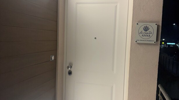 Une porte blanche avec une petite plaque au-dessus, une bande lumineuse sur le mur et une rambarde métallique sur la droite.