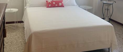 A bedroom with a bed, a nightstand, a small table, and a window.