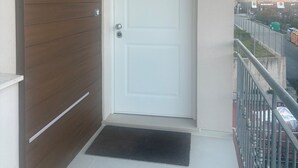 Une porte blanche avec une petite plaque au-dessus, un mur recouvert de panneaux de bois sur la gauche et une rambarde métallique sur la droite.