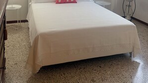 Une chambre à coucher bien rangée, avec un grand lit, une petite table de chevet, une commode, une fenêtre avec des stores et un luminaire fixé au mur.