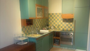 Une cuisine compacte avec des meubles de couleur turquoise, un dosseret à carreaux et un petit coin repas comprenant une table et des chaises.