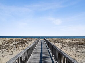 Una pasarela de madera que conduce a una playa con dunas y el océano al fondo.