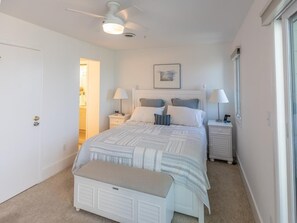 A bedroom with a bed, bedside tables, a bench, a ceiling fan, and a door. - Elegant 4BR Townhome w/ Bay Views & Pool Access (Fenwick Island)