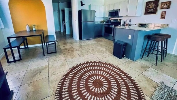 Een moderne keuken met een centraal eiland, een eethoek met een tafel en banken, en een vloerkleed met een patroon.