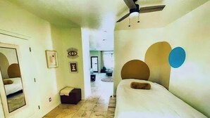 Een hotelkamer met een bed, een plafondventilator, een spiegel en een klein zithoekje.