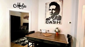 Een eethoek met een houten tafel en stoelen, een zwart-wit vloerkleed en een wanddecoratie met een silhouet en de tekst 'CASH'.